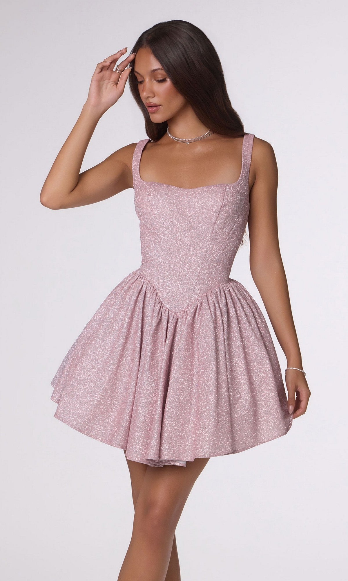 A woman poses against a plain light background in the Amoris T738 Short Homecoming Dress, a sleeveless fit-and-flare design in sparkly light pink stretch fabric, with one hand raised to her head.